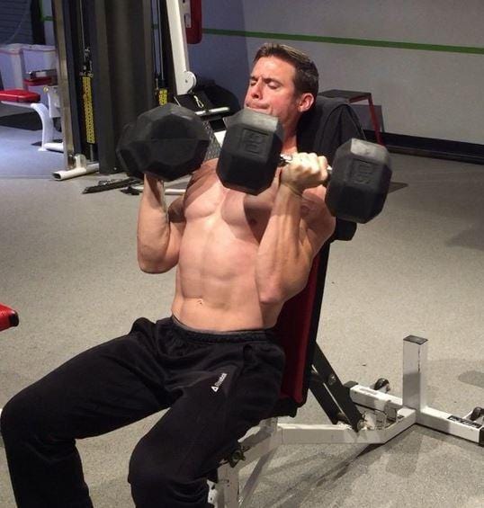 Man sitting on a bench pressing up heavy dumbbells