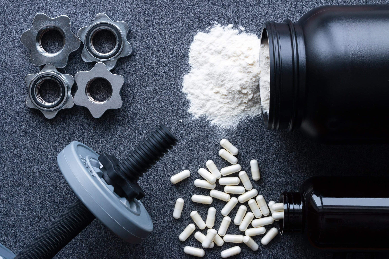 Little dumbbell, white capsules and white creatine powder on a grey background.