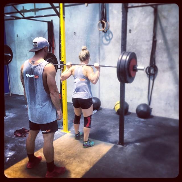 A guy spotting a girl performing a heavy back squat