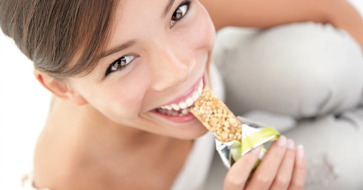 Young woman facing the camera while biting in a crunchy protein bar. 