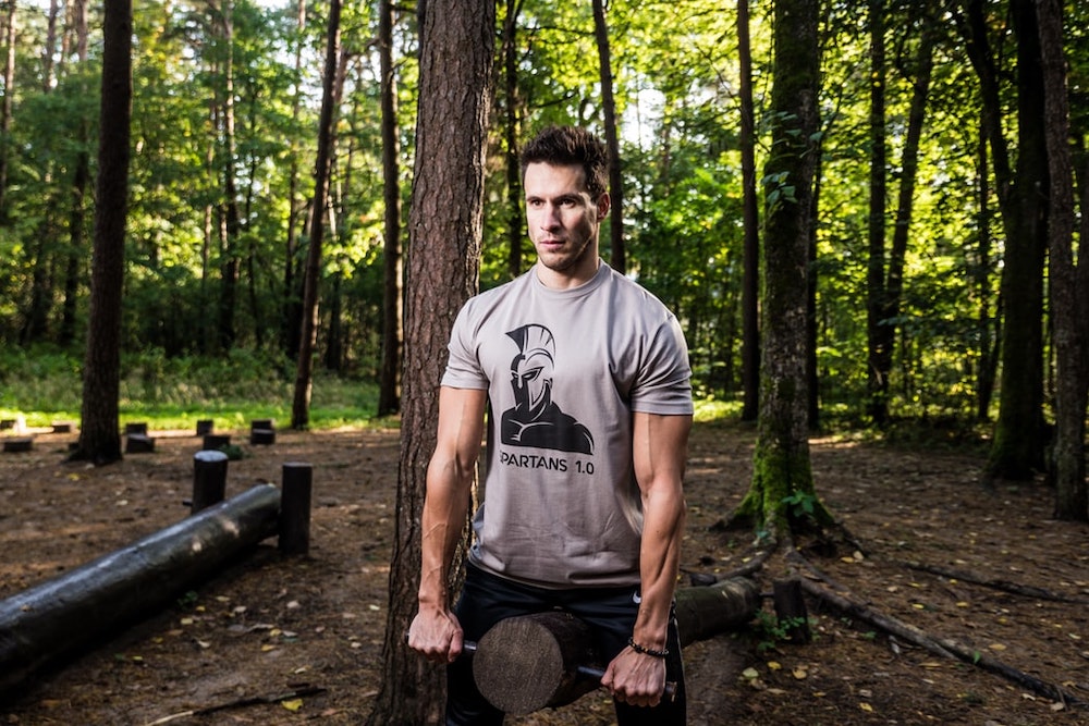A man exercising in the woods with tree trunk equipment 