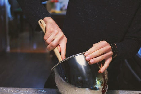 A woman's hands using a wooden utensil to stir in a metal mixing bowl