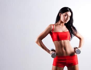 Women in good shape just wearing red sports bra and short pants while holding small dumbbell in her hands.